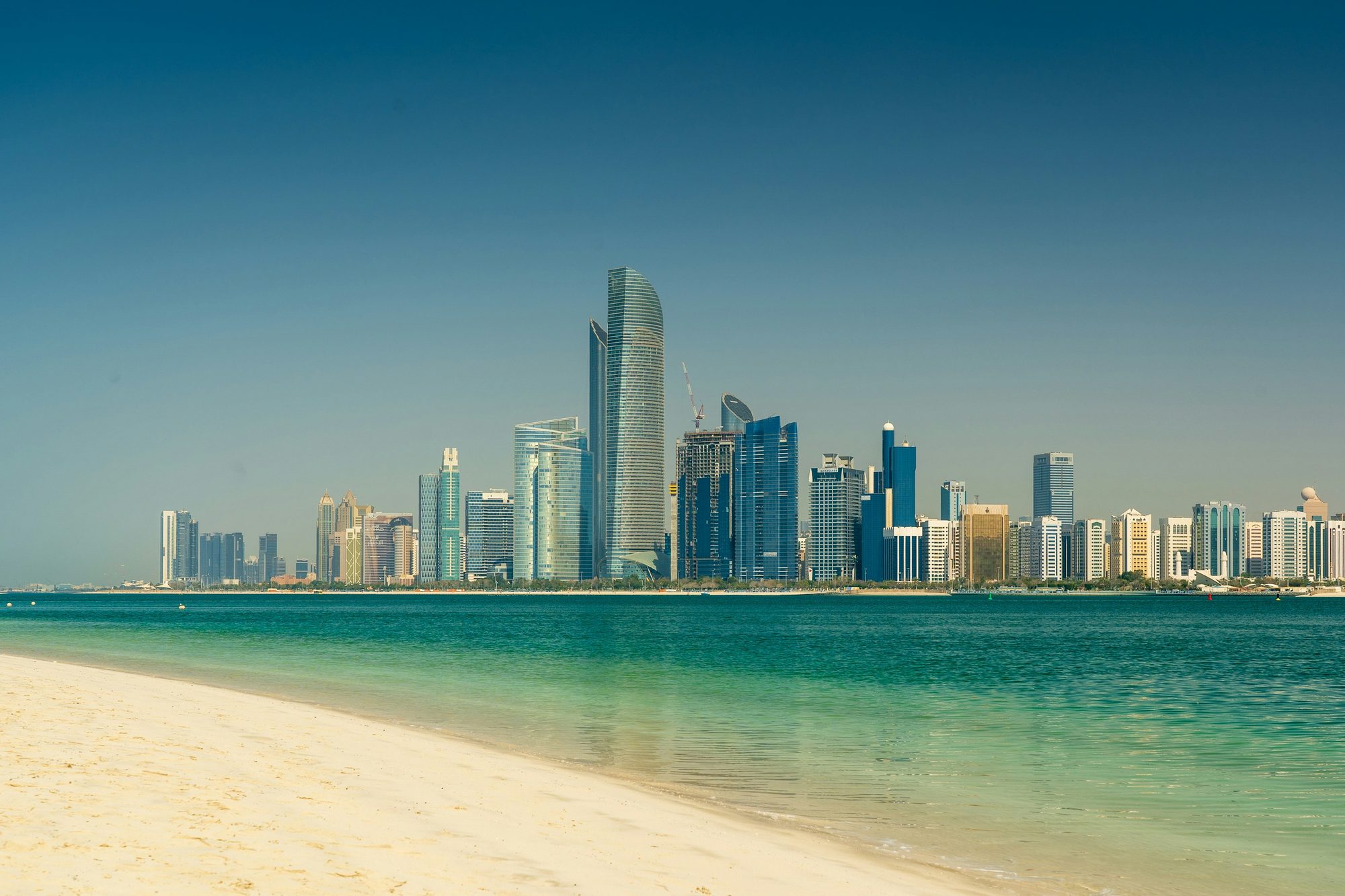 Abu Dhabin corniche-siluetti lasitorneineen nähtynä Arabianlahden kirkkaiden vesien yli valkoiselta hiekkarannalta.
